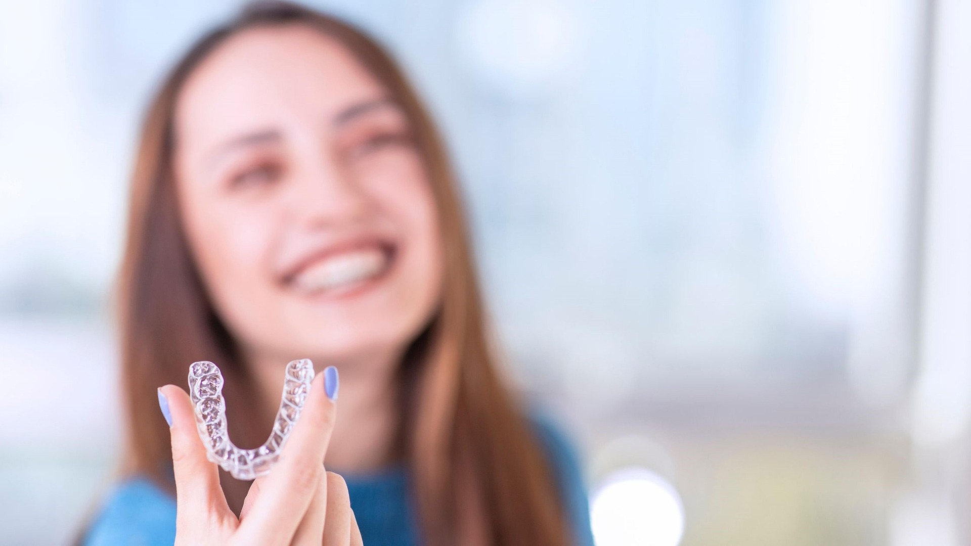 A smiling patient holding a clear aligner